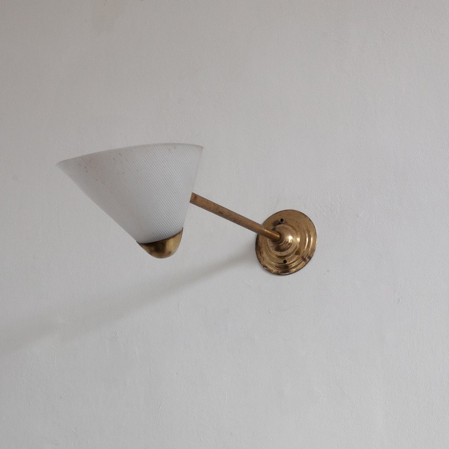 Wall-mounted lamp with white shade and gold fixture on a plain wall
