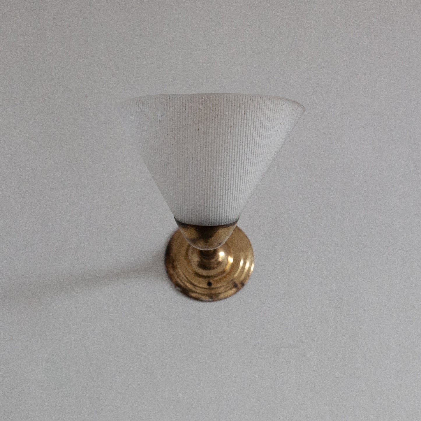 Small white lampshade with gold base on a plain background