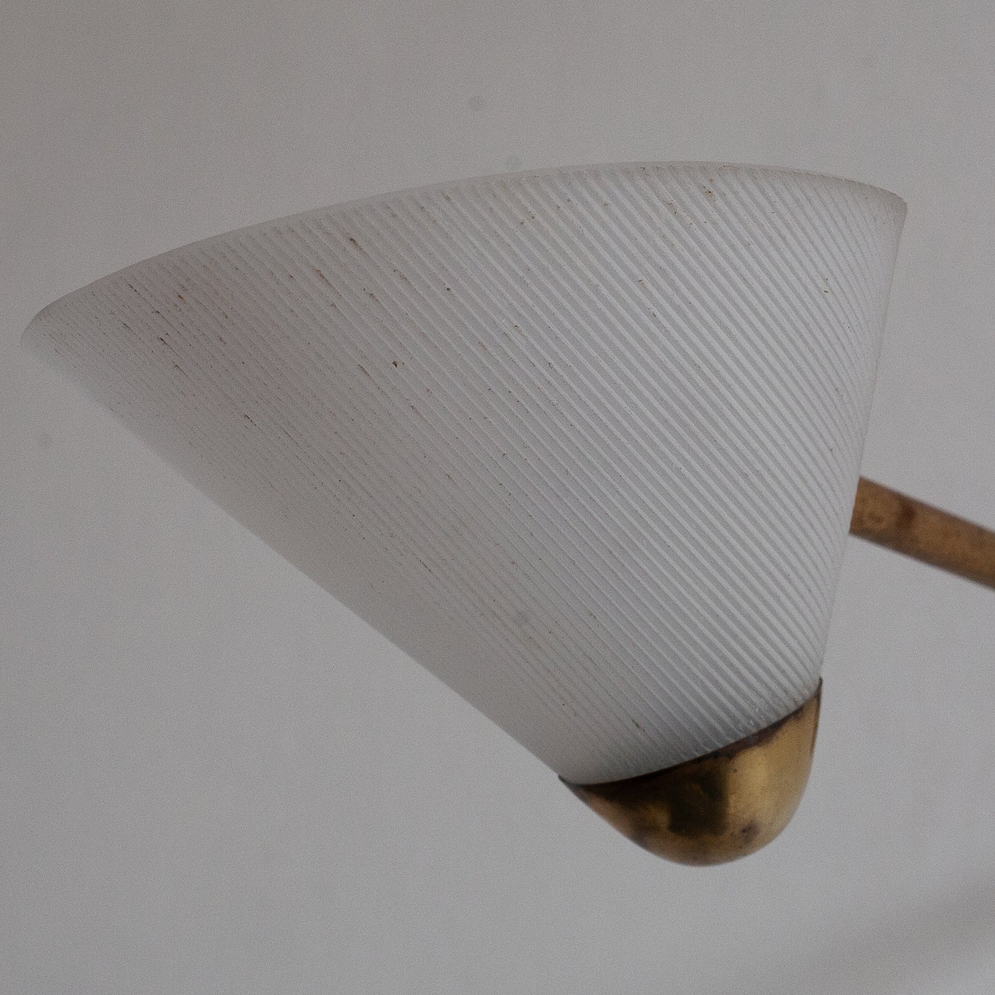 Light fixture with white cone-shaped shade and brass base on a plain background