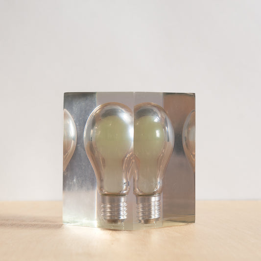 light bulb in a clear acrylic box on a beige surface with a white background