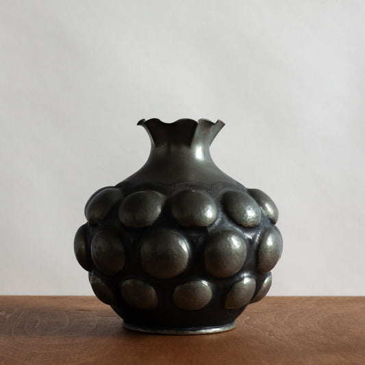 dark textured pewter vase on a wooden surface with a plain background