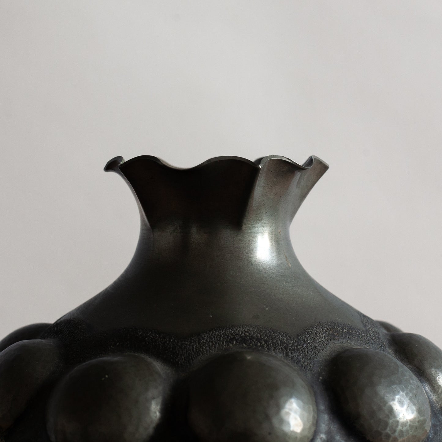 Black pewter vase with textured surface on a gray background