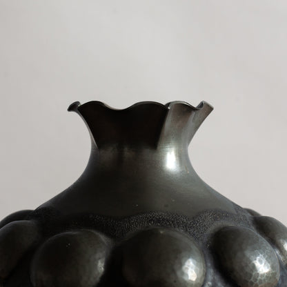 Black pewter vase with textured surface on a gray background