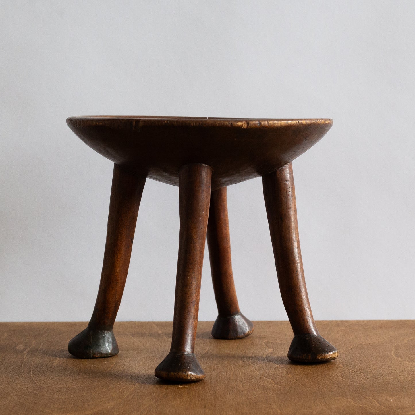 Wooden stool with four legs on a wooden surface and light gray background