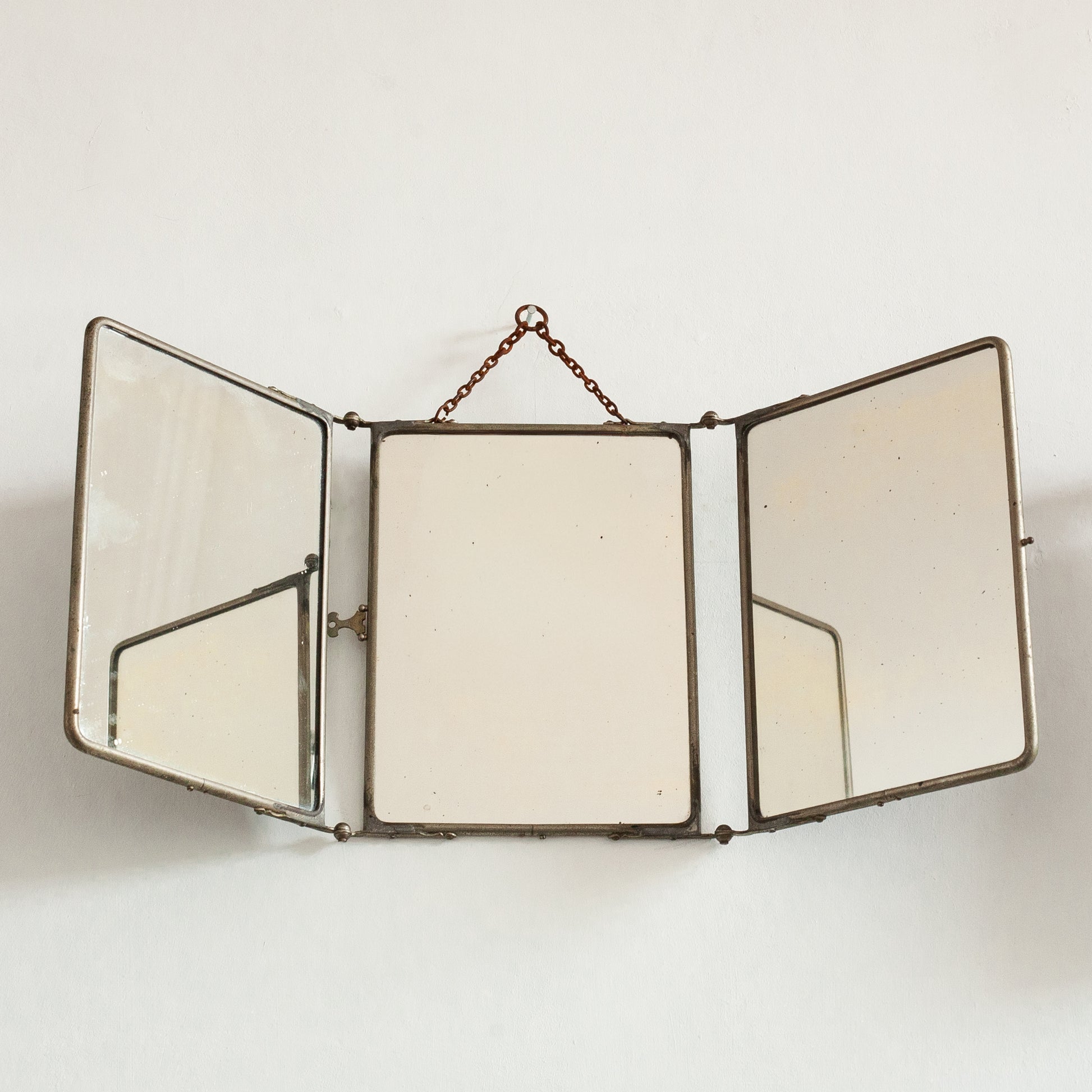 Triptych wall-mounted mirror with brass frame on a white background