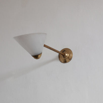 Wall-mounted lamp with white shade and gold fixture on a plain wall