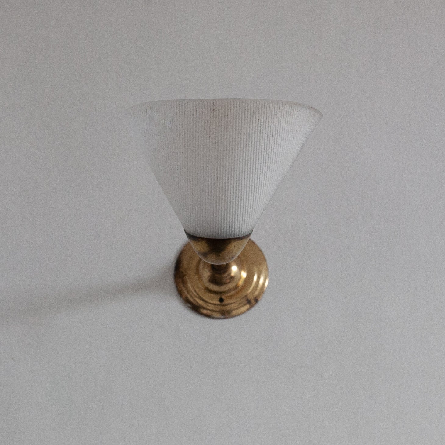Small white lampshade with gold base on a plain background