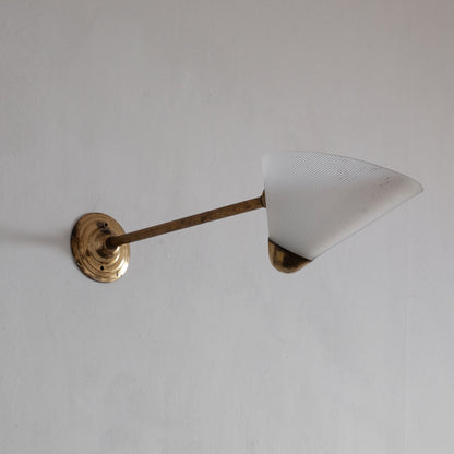 Wall-mounted light fixture with a cone-shaped white shade and brass arm on a plain background