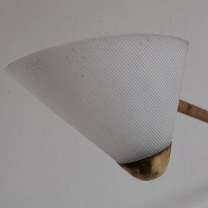 Light fixture with white cone-shaped shade and brass base on a plain background